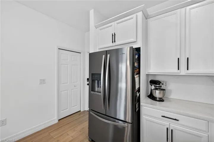 Kitchen featuring stainless steel refrigerator with ice dispenser, white cabinetry, light wood finished floors, and light stone countertops