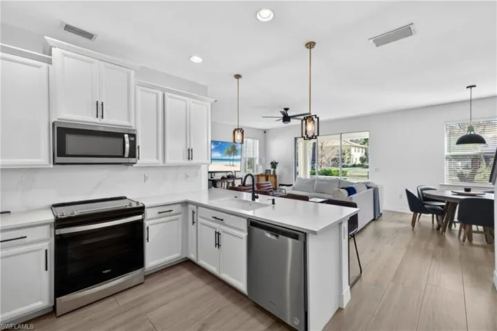 Kitchen with stainless steel appliances, white cabinetry, decorative light fixtures, open floor plan, and a peninsula