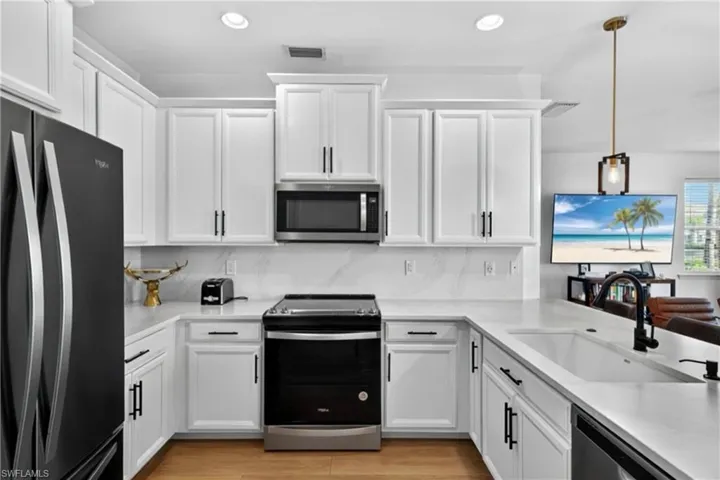 Kitchen featuring stainless steel appliances, white cabinets, and decorative light fixtures
