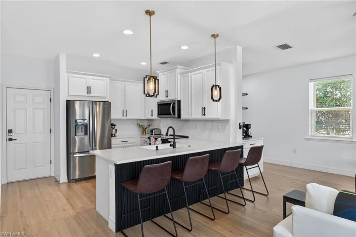 Kitchen featuring a peninsula, stainless steel appliances, light wood finished floors, white cabinetry, and a kitchen bar