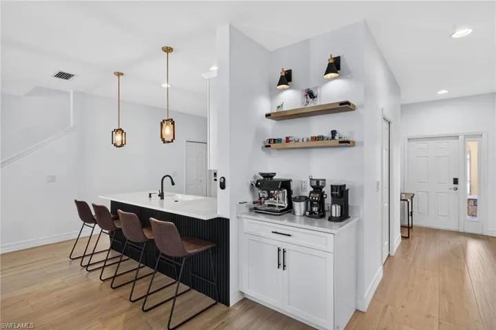 Bar area featuring light wood-style floors, open shelves, hanging light fixtures, and white cabinets