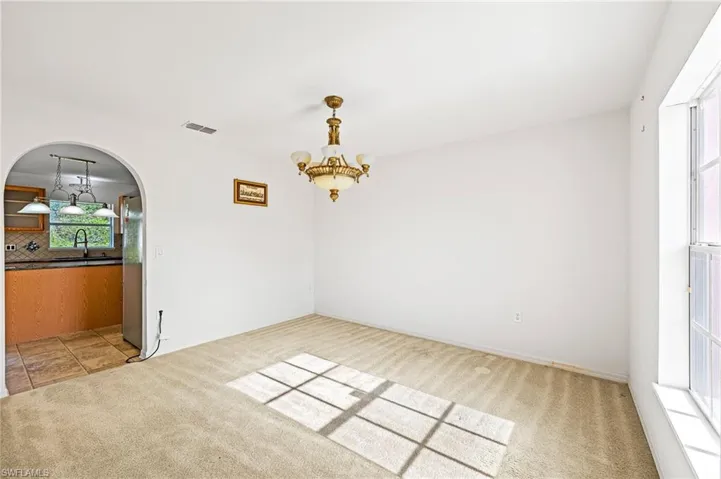 Unfurnished dining area featuring light carpet, arched walkways, a chandelier, and light tile patterned flooring