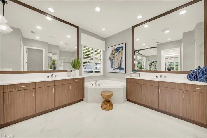 Full bath featuring a bath, two vanities, a stall shower, recessed lighting, and light marble finish flooring