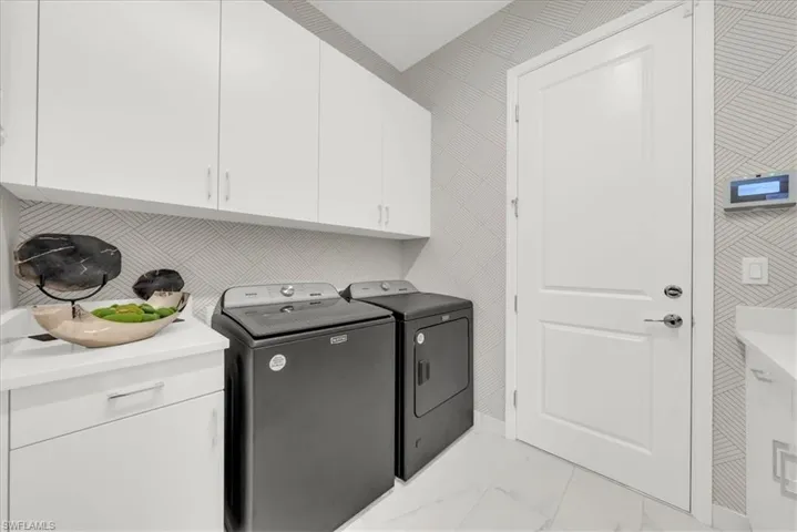 Washroom featuring light marble finish flooring, washer and dryer, and cabinet space