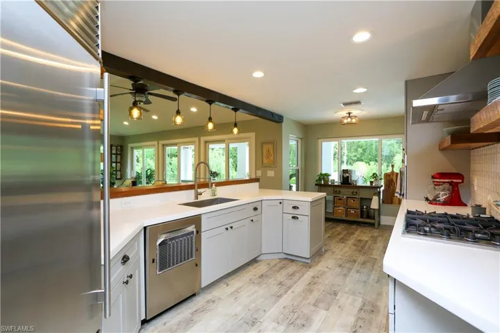 Kitchen with appliances with stainless steel finishes, light wood-style floors, recessed lighting, wall chimney range hood, and a peninsula