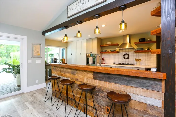 Bar with vaulted ceiling, tasteful backsplash, light wood-type flooring, extractor fan, and hanging light fixtures