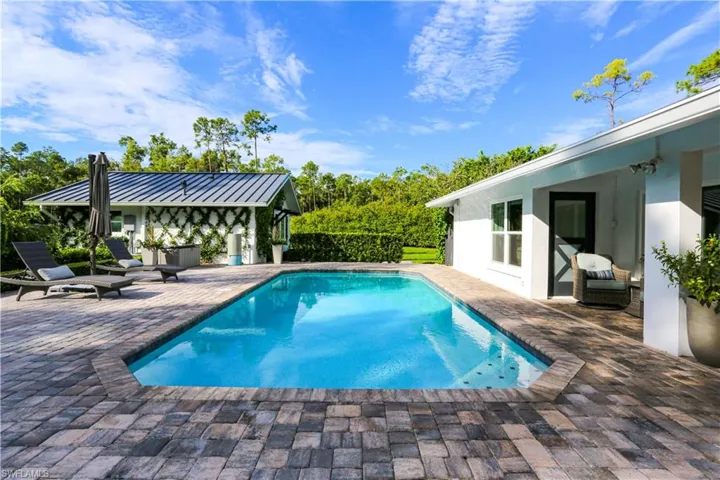 Outdoor pool with a patio area, an outbuilding, and view of wooded area
