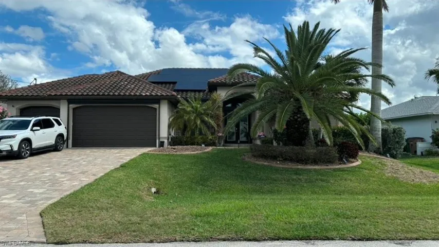 Mediterranean / spanish home featuring solar panels, a garage, driveway, a tiled roof, and a front yard