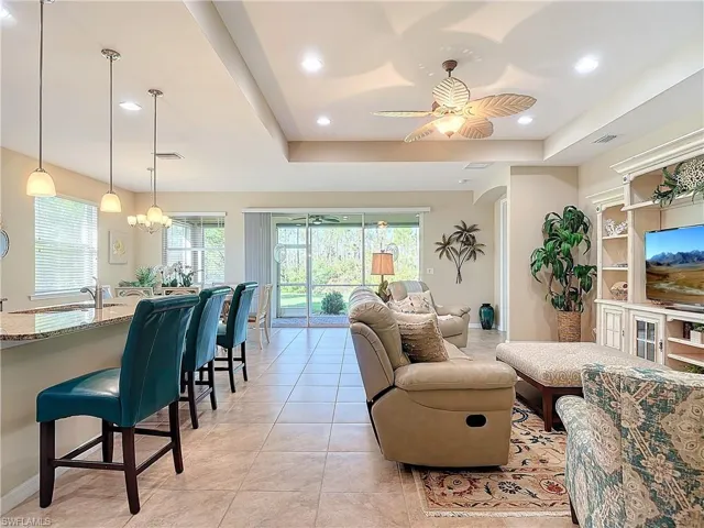 Living room featuring light tile patterned floors, a raised ceiling, sink, and ceiling fan with notable chandelier