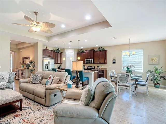 Living room featuring a tray ceiling, ceiling fan with notable chandelier, and light tile patterned floors