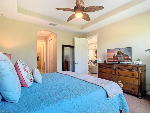 Carpeted bedroom featuring a raised ceiling and ceiling fan