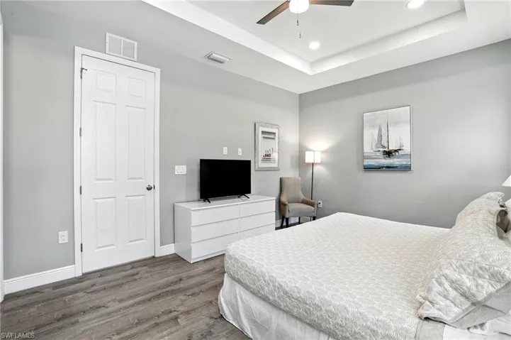 Bedroom with wood finished floors, a tray ceiling, ceiling fan, and recessed lighting