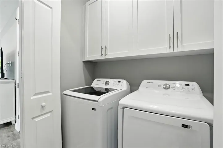Laundry area with washing machine and clothes dryer, cabinet space, and wood finished floors
