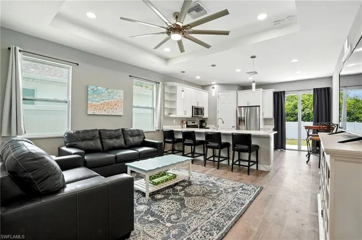 Living area featuring a raised ceiling, light wood-style floors, a ceiling fan, and recessed lighting