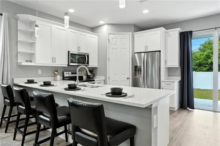 Kitchen with stainless steel appliances, white cabinets, a peninsula, a breakfast bar area, and recessed lighting