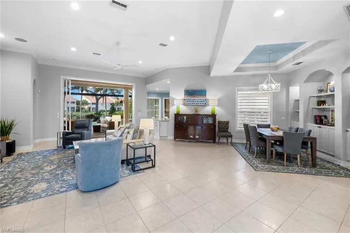 Living room featuring ceiling fan with notable chandelier, ornamental molding, and light tile patterned flooring