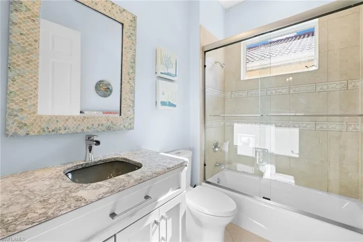 Full bathroom with tile patterned floors, vanity, enclosed tub / shower combo, and toilet