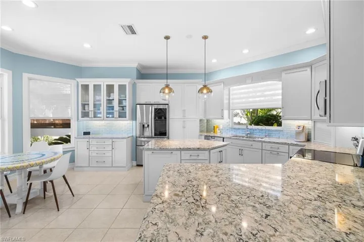 Kitchen with white cabinetry, light stone countertops, stainless steel fridge, pendant lighting, and a kitchen island