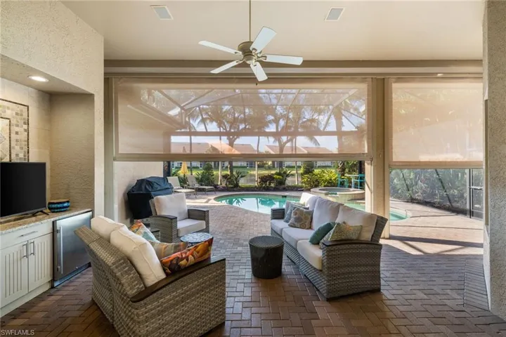 View of patio with glass enclosure, ceiling fan, outdoor lounge area, area for grilling, and a swimming pool with hot tub