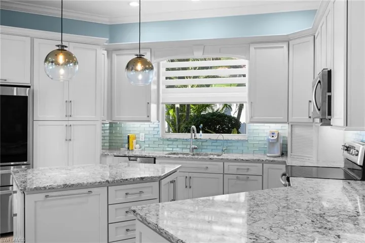 Kitchen featuring light stone countertops, appliances with stainless steel finishes, white cabinetry, and pendant lighting
