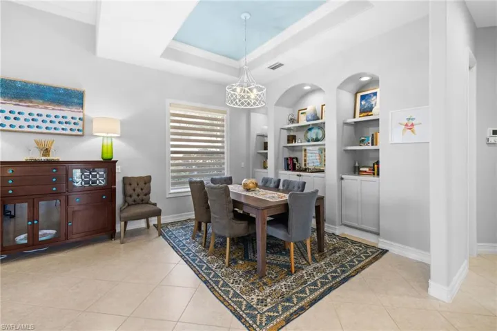 Dining room featuring built in shelves, light tile patterned floors, a raised ceiling, and ornamental molding