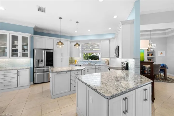 Kitchen with a center island, stainless steel appliances, pendant lighting, white cabinets, and ornamental molding
