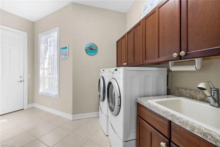 Washroom with cabinets, independent washer and dryer, light tile patterned floors, and sink
