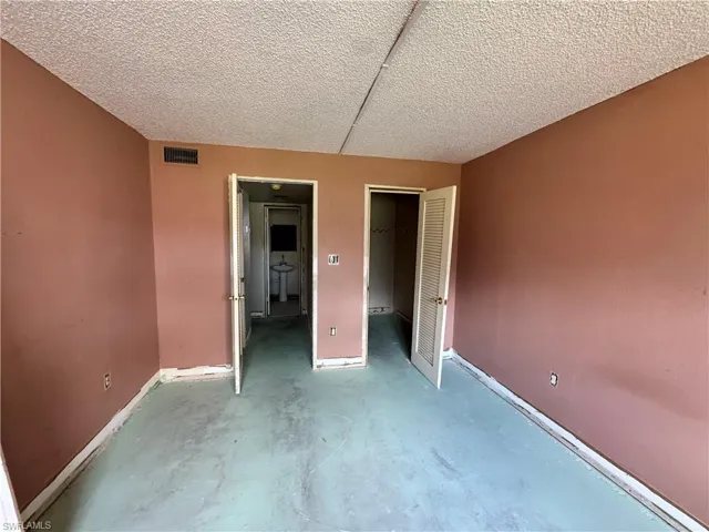 Unfurnished bedroom featuring a spacious closet, concrete flooring, and a textured ceiling
