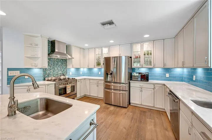 Kitchen with stainless steel appliances, light stone counters, recessed lighting, glass insert cabinets, and light wood finished floors