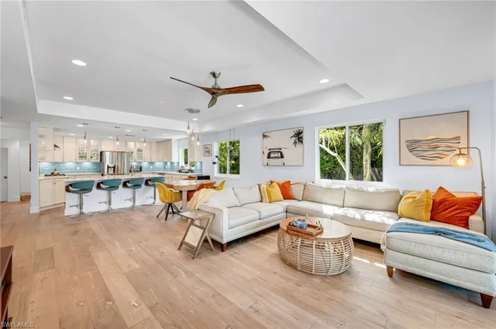 Living room featuring a tray ceiling, a ceiling fan, plenty of natural light, light wood-style floors, and recessed lighting