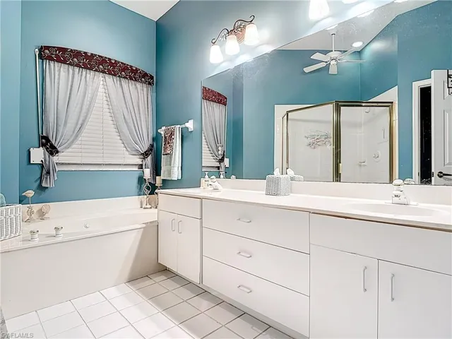 Full bath featuring a shower stall, a garden tub, double vanity, a ceiling fan, and a sink
