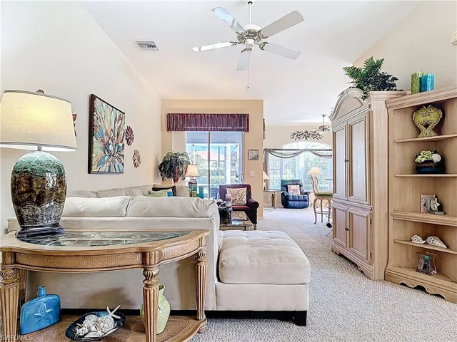 Carpeted living area featuring vaulted ceiling, visible vents, and ceiling fan