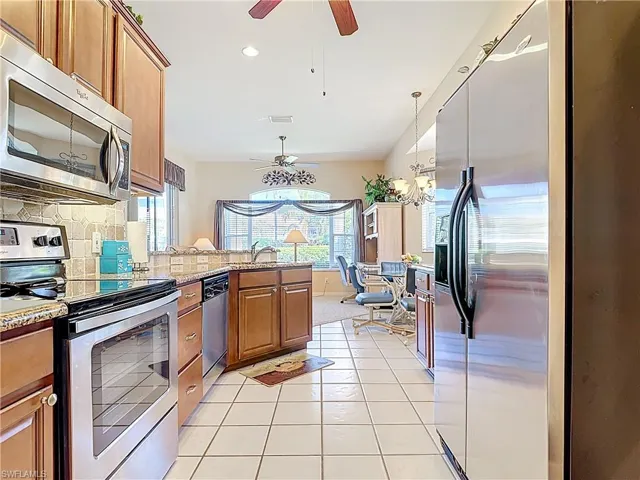 Kitchen with brown cabinets, a peninsula, appliances with stainless steel finishes, ceiling fan with notable chandelier, and tasteful backsplash