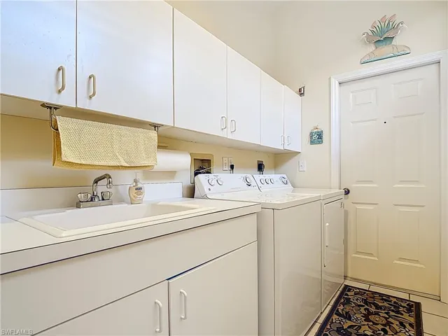 Laundry room with cabinet space, light tile patterned flooring, washing machine and dryer, and a sink