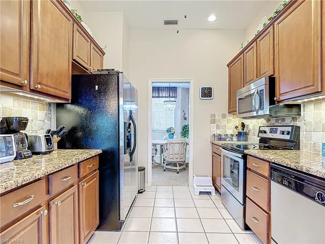 Kitchen with light tile patterned floors, light stone countertops, stainless steel appliances, tasteful backsplash, and brown cabinets
