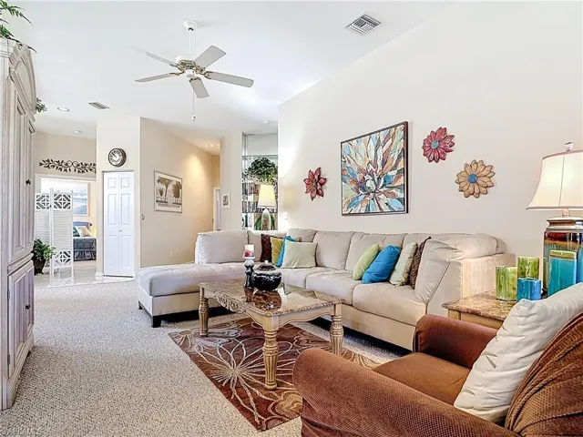 Living room with light carpet, visible vents, and ceiling fan