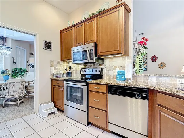 Kitchen featuring decorative backsplash, appliances with stainless steel finishes, brown cabinetry, and visible vents