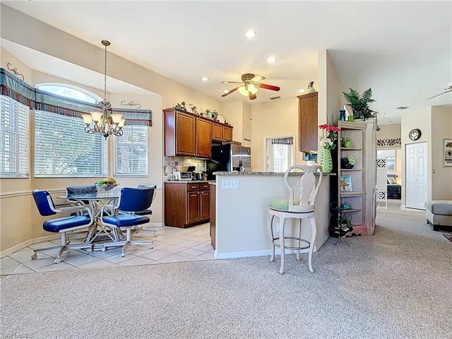 Kitchen with light carpet, ceiling fan with notable chandelier, a peninsula, freestanding refrigerator, and light tile patterned flooring