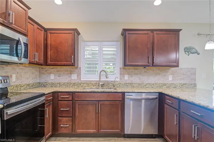 Kitchen with appliances with stainless steel finishes, sink, backsplash, hanging light fixtures, and light stone countertops