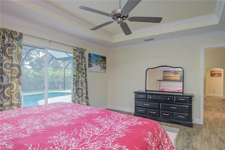 Bedroom featuring hardwood / wood-style flooring, ceiling fan, a tray ceiling, ornamental molding, and access to outside