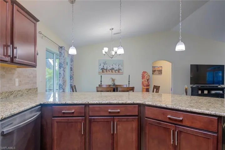 Kitchen featuring dishwasher, vaulted ceiling, decorative backsplash, and decorative light fixtures