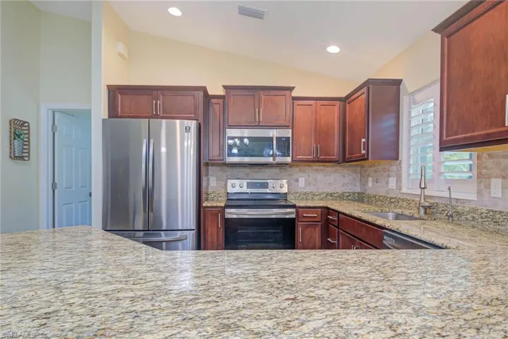 Kitchen featuring sink, appliances with stainless steel finishes, backsplash, light stone countertops, and vaulted ceiling