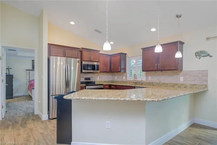 Kitchen featuring pendant lighting, appliances with stainless steel finishes, backsplash, vaulted ceiling, and kitchen peninsula