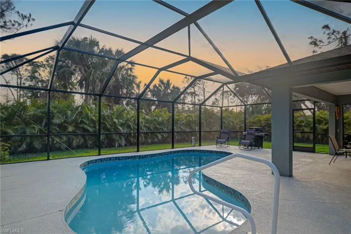 Pool at dusk featuring a patio area and glass enclosure