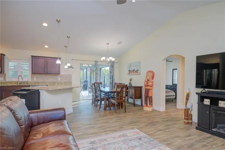 Living room with high vaulted ceiling, sink, light hardwood / wood-style floors, and a notable chandelier