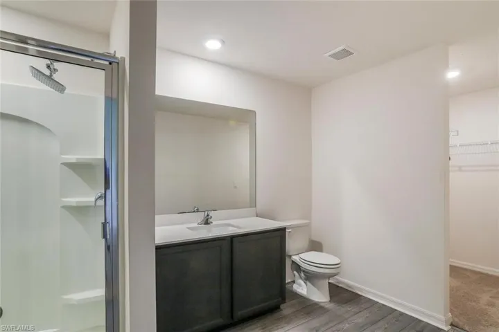 Bathroom featuring a glass-enclosed shower with built-in shelving, a double vanity with an integrated sink, a toilet, and wood-finish flooring