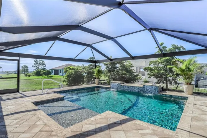 Screened outdoor pool area featuring a blue-tiled swimming pool with integrated waterfall features, a shallow sun shelf, and a paver patio surround