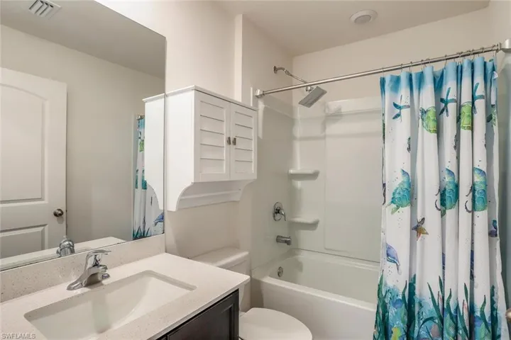 Bathroom featuring a tub/shower combination with a rainfall shower head, single vanity with a white rectangular sink, light-colored countertop, and a wall-mounted medicine cabinet