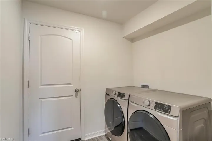 Laundry area featuring light neutral wall paint, wood-finish flooring, and a solid interior door with an arched panel