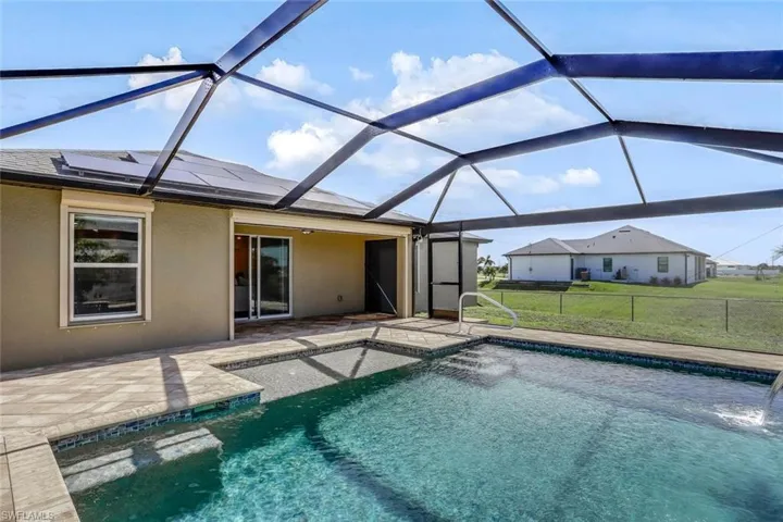 Screened-in pool area featuring a rectangular pool with integrated steps, tiled coping, and a water feature